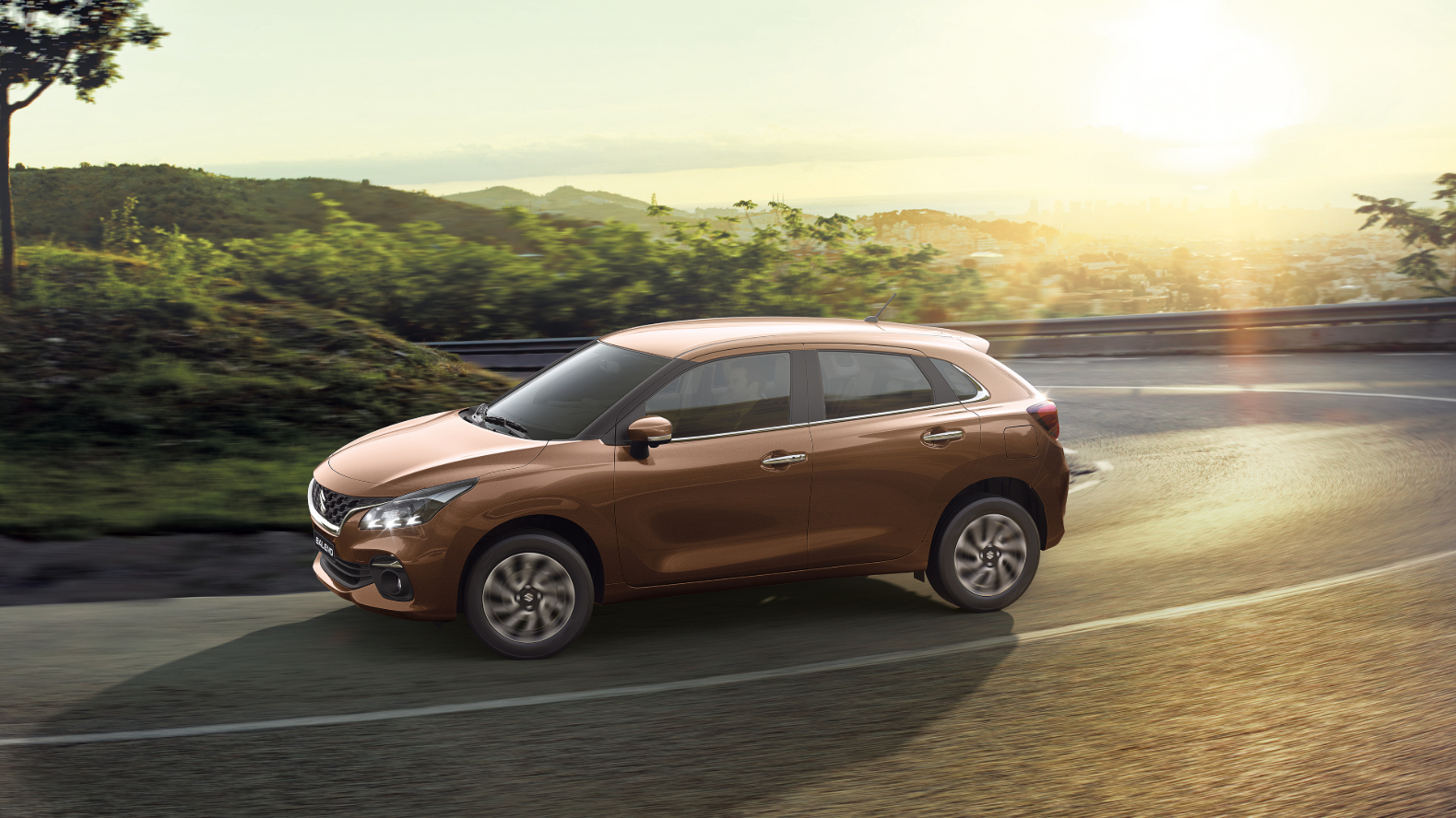 A Brown Suzuki Baleno driving down a curve in the road.